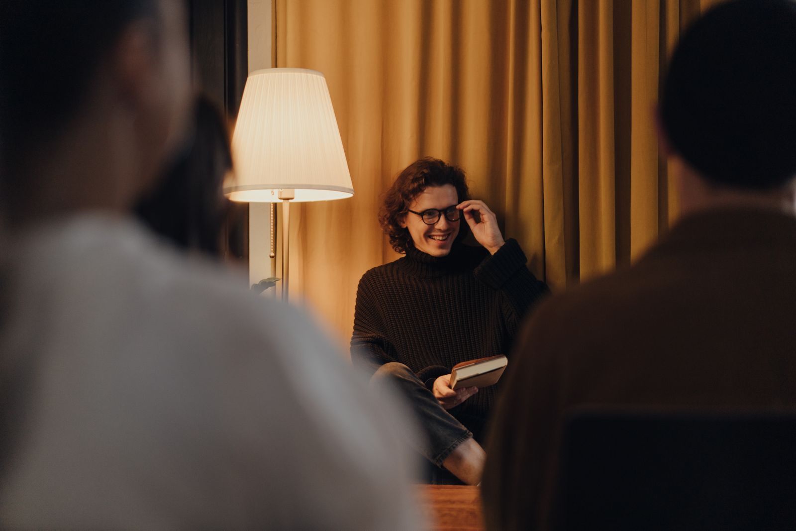 A woman reading aloud to a small audience in warm lamplight